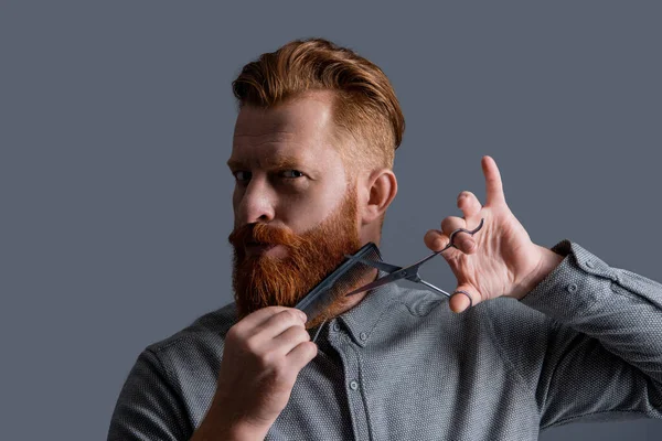 Kafkasyalı berber saç kesimi gri arka planda izole edilmiş. Makasla saç kesimi yapan adam. Adamın saç kesim stüdyosunda sakalı var. Adam tarıyor ve sakal kesiyor. Saç stili olan berber..