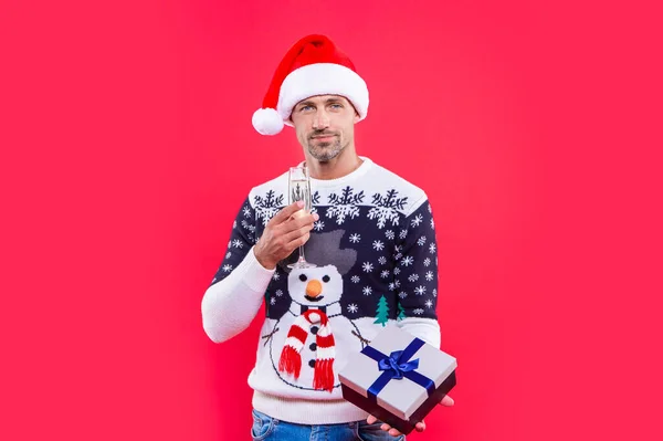 スタジオでクリスマスのプレゼントを持ってる クリスマスプレゼントとシャンパンの男 クリスマス サンタの帽子の男に贈り物とシャンパン 赤い背景に隔離されたクリスマスマン — ストック写真