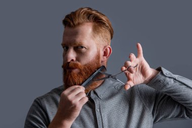 Saç stili olan berber. Berber adam saç kesimi gri arka planda izole edilmiş. Makasla saç kesimi yapan adam. Adamın saç kesim stüdyosunda sakalı var. Adam tarıyor ve sakal kesiyor..