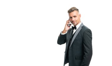 Smokinli neşeli adam beyaz arka planda izole bir şekilde telefonla konuşuyor..