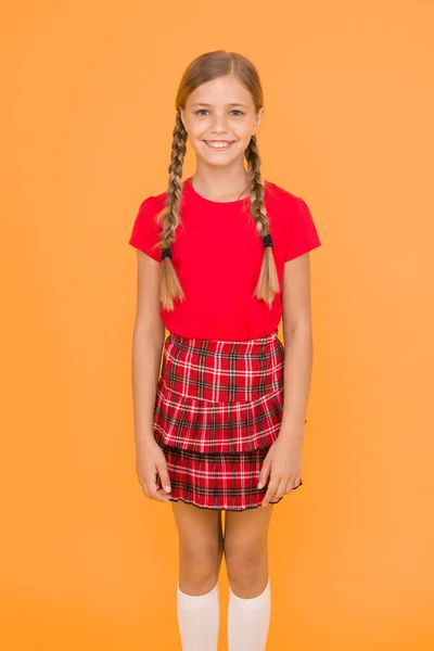 愛らしいキューティー 黄色の背景に魅力的なかわいい女の子の魅力的な笑顔 赤い服を着た幸せな小さな女の子 三つ編み髪の長い三つ編みの女の子 愛らしい女の子は 生徒であることを誇りに思っています 幸せな子供時代 — ストック写真