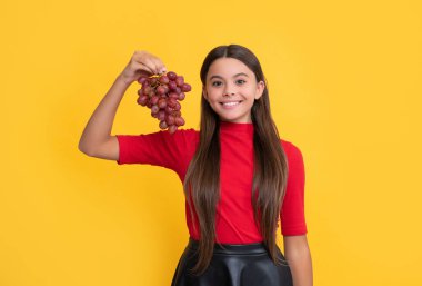 Gülümseyen çocuk sarı arka planda bir demet üzüm tutuyor..