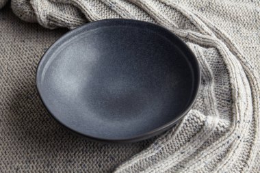 Hafif örülmüş yün bir kazağın arka planında boş siyah bir tabak. Tabağı hazırlamak için göster
