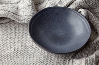 Hafif örülmüş yün bir kazağın arka planında boş siyah bir tabak. Tabağı hazırlamak için bir model