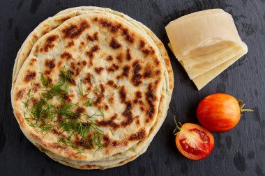 Peynirli, otlu ve siyah taş bir masada beyaz tabakta yoğurt soslu düz ekmek. Yukarıdan görüntüle