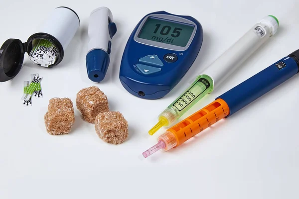 Glucosímetro, jeringa de insulina, azúcar morena sobre una mesa blanca —  Fotos de Stock