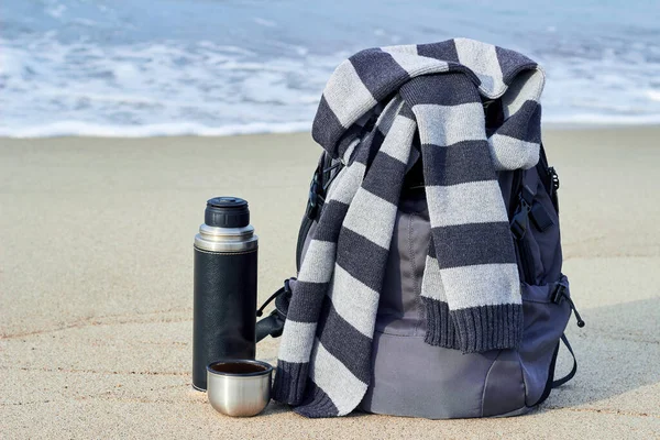 배낭, 줄무늬 스카프 서모, 모래 위의 뜨거운 커피 한 잔, 해변에서 스톡 사진