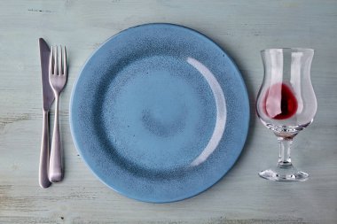 Açık mavi ahşap masada bir kadeh şarapla mavi tabak