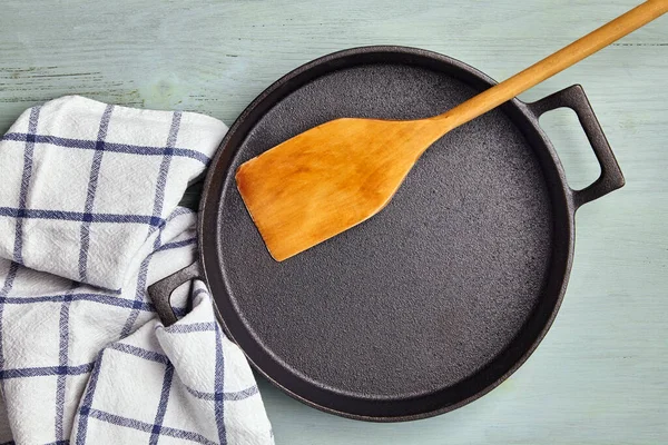 Boş yuvarlak dökme demir tava, ahşap spatula ve çay havlusu peçetesi.