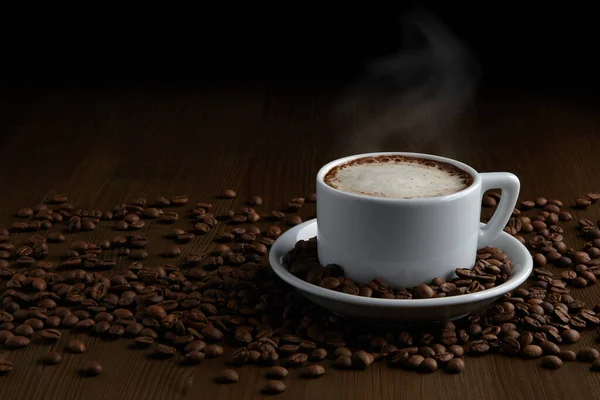 Une tasse de cappuccino chaud sur une soucoupe et des grains de café éparpillés — Photo