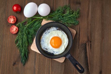 Küçük bir tavada kızarmış tavuk yumurtası standı, bir demet dereotu, vişneli domates.