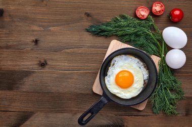 Küçük bir tavada kızarmış tavuk yumurtası standı, bir demet dereotu, domates.