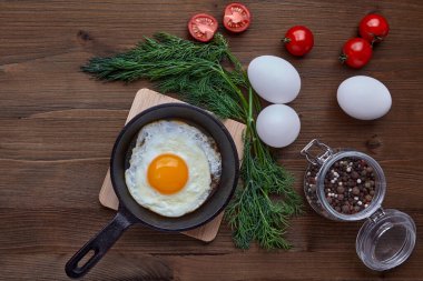 Küçük bir tavada sahanda yumurta, bir demet dereotu, domates.