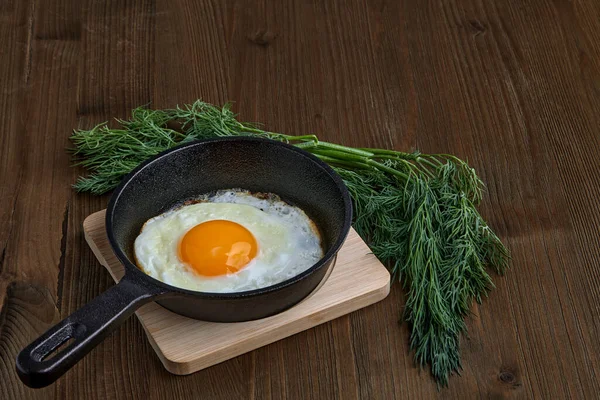 Huevo de pollo frito en una sartén pequeña con un soporte, un manojo de eneldo — Foto de Stock