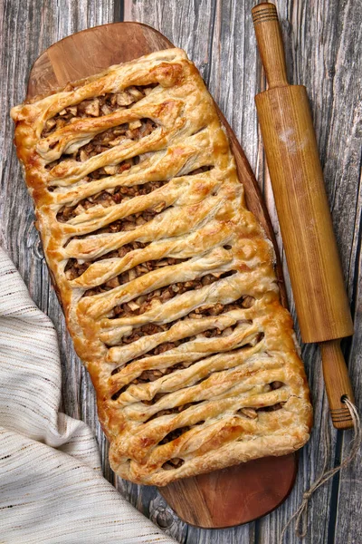 A wicker apple strudel pie with walnuts lies on a cutting board — 图库照片