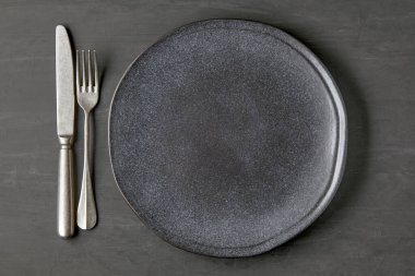 Koyu beton arka planda, çatal bıçaklı siyah bir plaka.