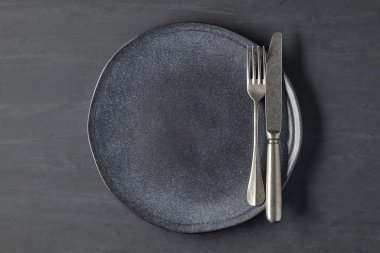 Koyu beton arka planda, çatal bıçaklı siyah bir plaka.