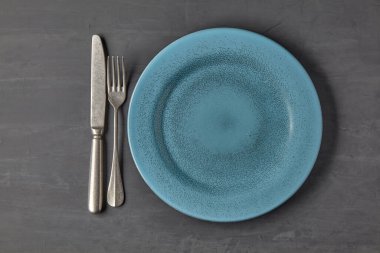 Koyu beton arka planda, çatal bıçaklı mavi plaka.