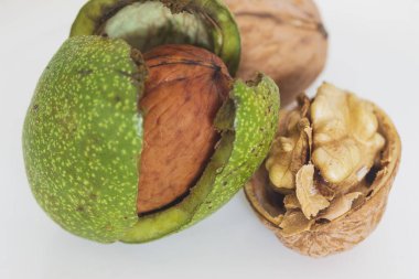 Çatlamış yeşil kabuklu olgun ceviz ve gri-beyaz arka planda yarım ceviz makrosu.