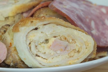 Dilimlenmiş sosis ve dilimlenmiş rulo köfte parçaları beyaz bir tabakta, makro kenarlı bir manzarada.