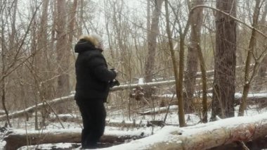 Bir adam doğayı eski bir film kamerasıyla karlı bir ormanda devrilmiş ağaçların arasında fotoğraflıyor.