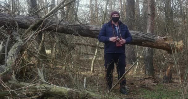 倒れた松の木を背景にヴィンテージフィルムカメラを持った写真家が森を調べ — ストック動画