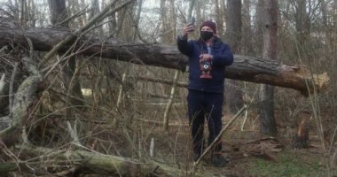 Düşen bir çam ağacının arka planında eski bir film kamerası olan bir adam selfie çeker..