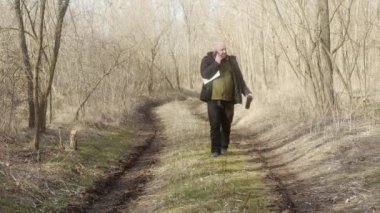 Kolunun altında dizüstü bilgisayarı olan bir adam ormanda cep telefonuyla duygusal olarak konuşuyor..