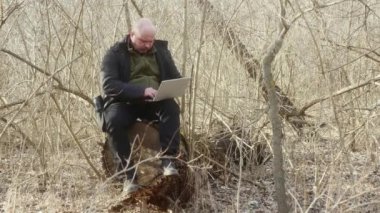  Yoğun bir ormanda dizüstü bilgisayarın üzerinde oturan serbest çalışan biri. Uzak çalışma konsepti.