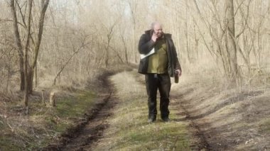  Kolunun altında dizüstü bilgisayarı olan mutlu bir adam ormanda cep telefonuyla konuşuyor.