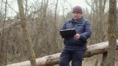 Doğada bir adam devrilmiş bir çam ağacında otururken tabletine bakar..