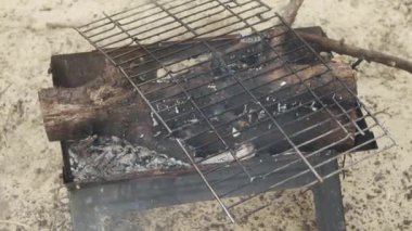 Kalın dalları yanan ızgaralı bir kamp barbeküsü..
