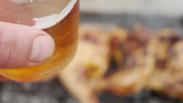 Mano Sostiene Vaso Plástico Con Cerveza Sobre Las Patas Pollo — Vídeo de stock