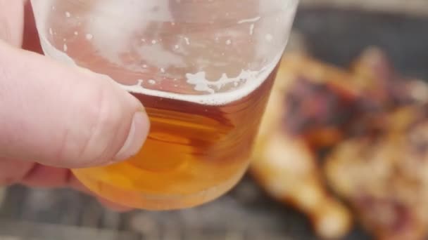 チキンの足の上にビールが付いているプラスチック製のガラスは屋外で焼かれ — ストック動画