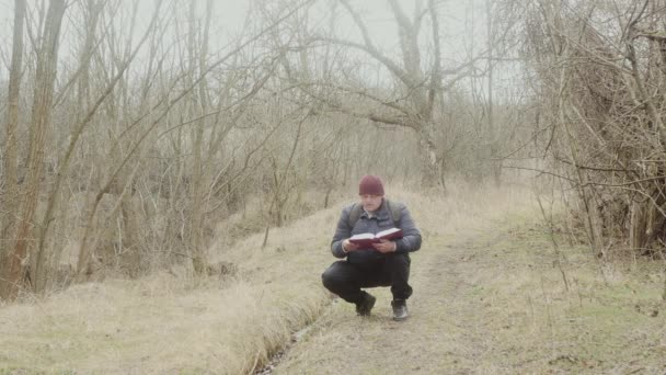 Muž Čte Tlustou Knihu Když Dřepí Lesní Cestě — Stock video