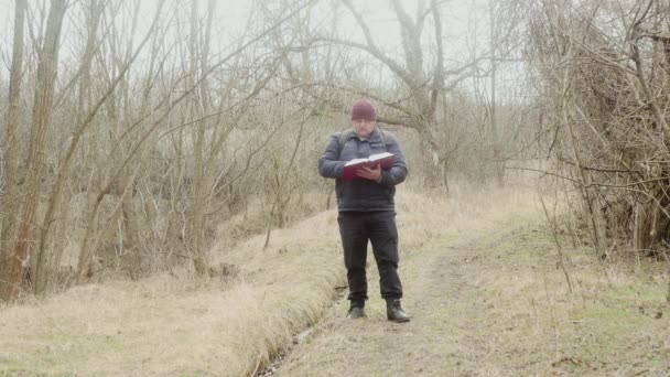 ある男が森の小道で太い本を読み — ストック動画