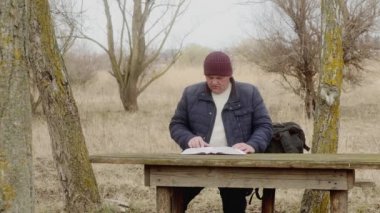  Adam doğada, kitap okuyor ve sayfayı çeviriyor, ahşap bir masada oturuyor..