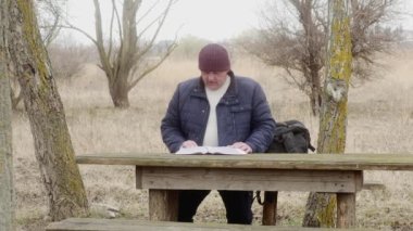 Bir turist, ormanda devrilmiş bir çam ağacında oturan Ortodoks İncili 'ni okur.