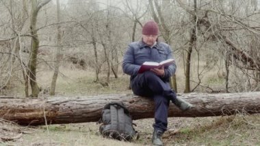 Bir turist, ormanda devrilmiş bir çam ağacında oturan Ortodoks İncili 'ni okur.