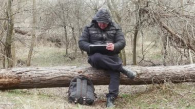 Bir gezgin, hafif bir kar yağışı sırasında ormandaki bir çam ağacında oturan trafo bilgisayarında bir şeye bakar.