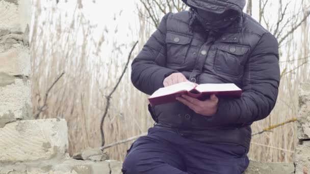 Mężczyzna Kapturem Głowie Uważnie Czyta Grubą Książkę Siedząc Zawalonej Ścianie — Wideo stockowe