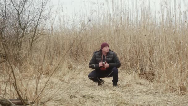 一个蹲在大自然中的男人 靠着春天里的芦苇 用老式胶卷照相机拍照 — 图库视频影像