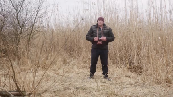 自然界の男が早春の湖の葦を背景にヴィンテージフィルムカメラで写真を撮り — ストック動画