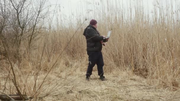 一位旅行者正在湖中芦苇的背景下 用一台装有老式摄像机的笔记本电脑在他的脖子上打字 — 图库视频影像