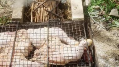 Bir adam ızgaranın yanında çiğ tavuk budu ve patatesle ateş yakar..