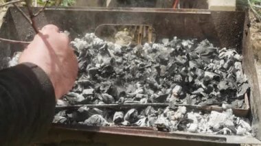 Dalı olan bir el barbeküde kömür karıştırır..