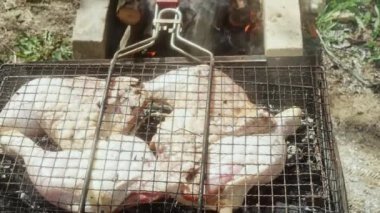  İştah açıcı taze çiğ bacaklar, yanan odunlu bir çukurun yanındaki ızgarada hazırlanıyor..