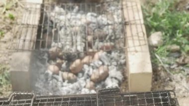 Patates, sıcak kül dolu bir çukurda pişer, tavuğun yanında, kabuklu, yakın plan.