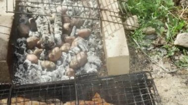 Potatoes are baked in hot ash, near chicken legs with Appetizing Crust, close -up.
