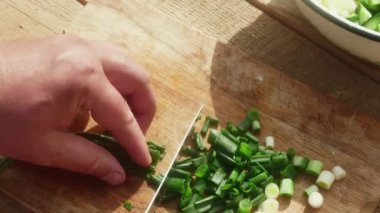  a hand with a knife cuts a leek on a wooden board for a spring salad.